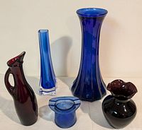 Seven antique and vintage glass pieces including cobalt blue tall vase, slender cobalt vase, ruby red jug, and black amethyst vases with ruffled rims.