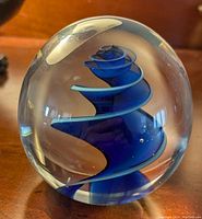 Clear spherical art glass paperweight with blue spiral internal design, signed Bush 1990, about 3 inches tall.