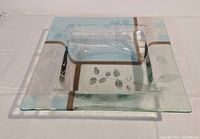 Top angle view of the square fused glass dish showing leaf motifs, pale blue and brown accents on a clear glass body.