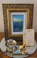 Shot of the framed watercolor, small silver-faded bowl, gilded porcelain deer figurine, and gold floral menu card on a mirrored surface