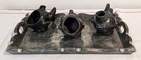 Photo of three black pottery vessels arranged on the hammered tin tray, showing shapes and handles of each pottery piece.