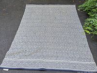 Geometric patterned black and white rectangular cotton rug laid out on solid surface, showing front side with border and main pattern distinct.