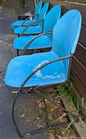 Side view of four vintage Steelcase stacking chairs in blue showing wear and paint loss on molded seats, tubular steel armrests and frames.
