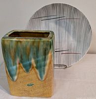 Shallow round pottery bowl with Prim Rose pattern in front of the rectangular drip glaze pottery vase