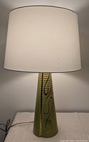 Full view of mid-century modern table lamp with chartreuse ceramic base and off-white fabric lampshade.