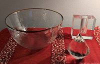 Photo of the three items showing the large hammered texture crystal bowl with gold rim, cubist clear glass bud vase, and geometric Tiffany cut crystal paperweight on a red textile.