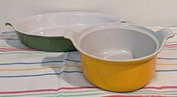 Two casseroles on a striped cloth: green oval stoneware baker by Emile Henry and yellow enameled cast iron baker by Le Creuset