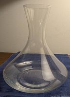 Clear blown glass carafe with wide base and narrow neck, set on a dark blue cloth, showing overall shape and transparency