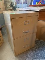 Front view of beige two-drawer metal filing cabinet closed, showing drawer handles and label holders.