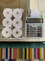 Photo of the Canon calculator with paper roll and the full box of six paper rolls beside it on the table.