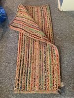 Folded large colorful throw rug showing woven straw base with multicoloured fabric strips and texture.