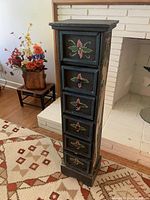 Front view of the black painted wooden chest with six drawers, each drawer adorned with painted floral designs in red, green, and cream.
