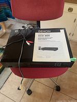 Denon stereo CD player DCD-800 on red chair with power and audio cables and instruction manual on top.