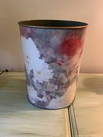 Front and side angled view of round metal wastebin showing floral Monet-like artwork and gold/brass rim.