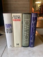 Four hardcover novels standing upright showing titles on spine and front covers in good condition.