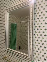 Large rectangular wall mirror with ornate multi-layered frame, positioned against wallpaper with cloverleaf pattern.