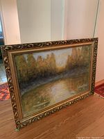 Full view of the framed painting depicting a forest pond with autumn colors and a boat on water.