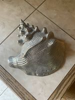 Top-down view of silver-colored metal seashell showing detailed texture and ridges.