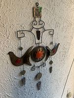 Front view of metal wall mobile with birds and hanging discs on textured wall.