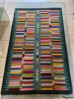 Full top view of rectangular multicolored wool rug on tile floor showing vibrant geometric pattern with dark green border.