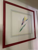 Bright red framed pastel flower print, full view showing frame and artwork.