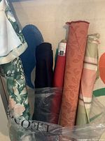 Photo of five fabric rolls standing upright showing variety of colors and patterns including black, red, orange floral jacquard, striped mint green and peachy pink, and floral garden print