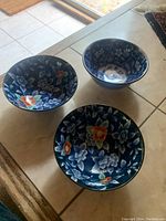 Three Chinese bowls arranged on tile floor showing floral patterns inside.