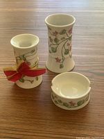 Three small German porcelain items with floral vine and flower design displayed on wood surface. Candle holder decorated with bow, taller vase and ashtray.