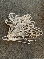 Pile of twenty white plastic hangers on carpet, showing overall quantity and color
