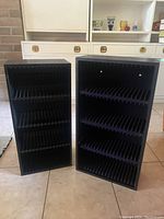 Two black wooden shelves with multiple slots for CD storage, shown side by side.