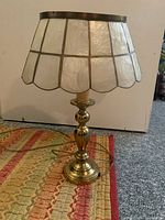 Full view of brass bedside table lamp with stained glass shade on a patterned rug with wall background.