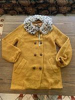 Yellow knit sweater laid flat showing buttons, pockets, and overall length with fur collar.