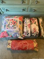 Three decorative throw pillows arranged on carpeted floor in front of a dresser. Two square pillows with floral patterns and one red paisley bolster pillow.
