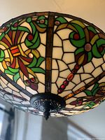 Close-up of stained glass shade showing green vine motifs and red jewel accents