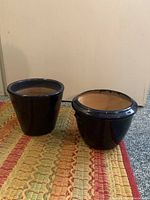 Two navy blue flower pots placed side by side on a colorful woven rug, showing exterior with glossy finish and shape difference.