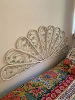 Full view of the wicker wall hanging or potential headboard, showing the semi-circular fan shape with floral motifs above a colorful bedspread.