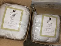 Two white Concierge Collection Super Loft™ mattress pads, new in packaging, inside cardboard boxes.