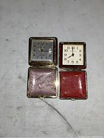 Two vintage square pocket watches inside open protective cases showing dial details and interior linings.