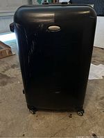 Photo of large black hard shell suitcase front view with visible scratches on surface and four spinner wheels on bottom.