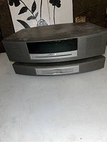 Front view of Bose Wave Music System main unit and detachable speaker showing gray front grille and display panel.