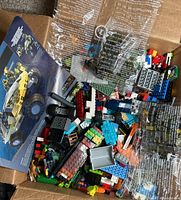 Cardboard box with bagged LEGO pieces, loose bricks, and instruction manual visible