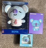 Photo showing BT21 Koya plush in box, Koya coin bank box, and Koya mini speaker box on carpeted floor.