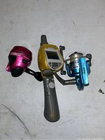 Top view showing two fishing reels and one fish finder device on white background.
