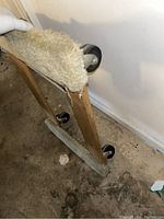 Angle view of wooden furniture dolly with carpeted platform and visible caster wheels on the floor.