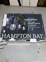 Box of Hampton Bay LED string lights 24 ft, commercial grade, plug-in, shatter resistant LED filament bulbs, 12 bulbs, suitable for outdoor use.