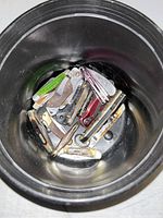 Top view photo inside black container showing over 10 small pocket knives and multi-tools with various handle colors and metal blades.