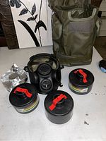 Military gas mask with three cylindrical filters and a green carrying bag