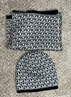 Photo showing a Michael Kors knit skully and matching scarf on carpeted floor, both featuring repeating 'MK' pattern in black and white.