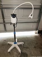 Full view of mobile teeth whitening machine on 5-wheel base, adjustable pole, flexible arm with LED light head.