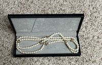 Photo showing a double-strand pearl necklace with gold decorative accents inside a black jewelry box with gray lining.